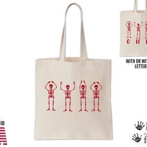 May include: A white canvas tote bag with red skeleton figures holding their hands above their heads. The skeletons are arranged to spell out "OHIO". The bag is available with or without the letters.