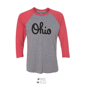 May include: A gray and red baseball tee shirt with the word "Ohio" in black script on the front.