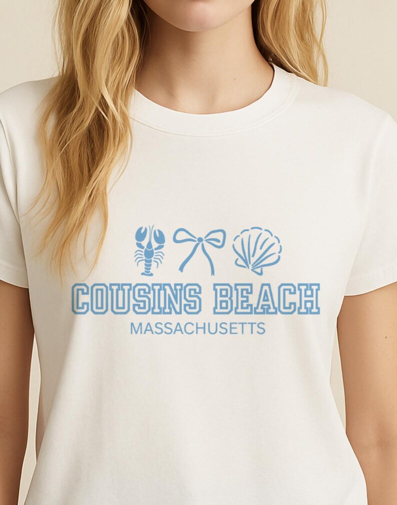 Op de afbeelding: Wit T-shirt met een lichtblauwe afbeelding van een kreeft, strik en schelp. De tekst "COUSINS BEACH MASSACHUSETTS" staat eronder in lichtblauw gedrukt. Ronde hals.