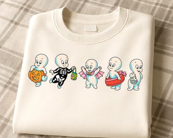 May include: Cream-colored sweatshirt featuring a graphic of five cartoon ghosts in Halloween costumes. One ghost holds a jack-o'-lantern, another is in a skeleton costume, and others wear a bat costume, a red inner tube, and hold a basket.