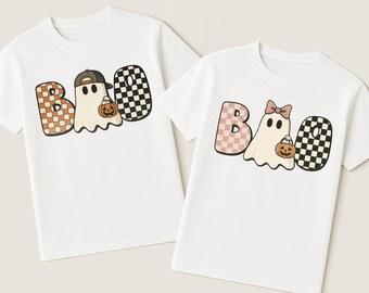 May include: Two white t-shirts with the word "BOO" in a playful Halloween design. One shirt features a ghost wearing a baseball cap and holding a pumpkin. The other shirt has a ghost with a bow and a pumpkin.