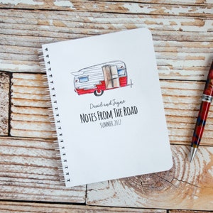 May include: A white notebook with a red and white illustration of a vintage camper on the front cover. The text "David and Jayne NOTES FROM THE ROAD SUMMER 2017" is printed below the illustration.
