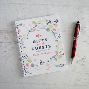 May include: A white spiral bound notebook with a floral design and the text "Gifts and Guests To Honor Mom-To-Be Kate Wilson".