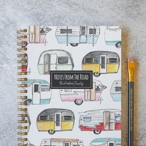 May include: A white spiral bound notebook with a colorful pattern of vintage camper vans. The cover reads "Notes from the Road" and "The Parker Family".