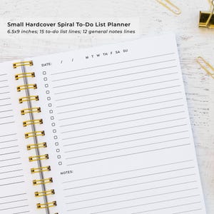 a spiral-bound notebook with a blank page, accompanied by a stapler and a pair of gold binder clips on a wooden surface.