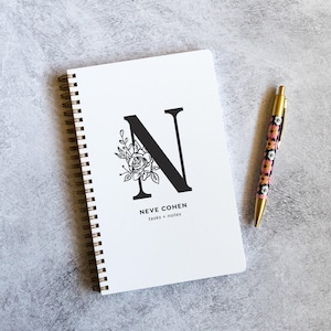 May include: A white ceramic mug with a black handle and the text "But First, Coffee" in a black, handwritten-style font. The mug is on a white surface.