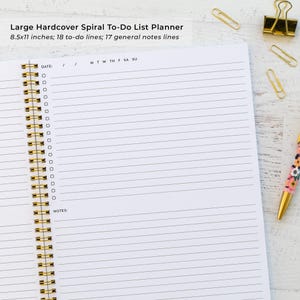 a spiral-bound notebook with a blank page, a pen, and some office supplies such as a stapler and binder clips, all arranged on a white surface.
