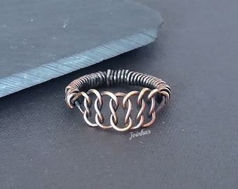 Puede incluir: Un anillo de cobre hecho a mano con un diseño único de cota de malla. El anillo presenta una serie de eslabones interconectados, creando un patrón intrincado. El anillo es una mezcla de cobre y metal oscuro, con la palabra "Joinhas" visible.