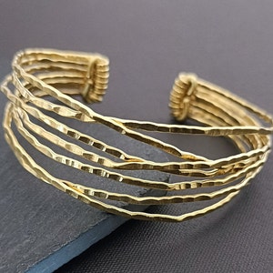 May include: Gold-toned metal bracelet with a hammered finish. The bracelet is made of multiple strands of wire that are woven together.