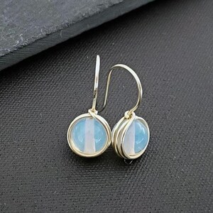 May include: A pair of silver dangle earrings with a light blue and white gemstone. The earrings are made with wire wrapped around the gemstone.