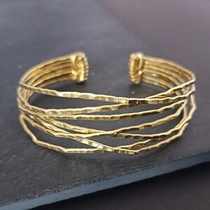 May include: A gold-toned multi-strand bangle bracelet with a hammered finish. The bracelet is made of five thin bands of metal that are woven together.