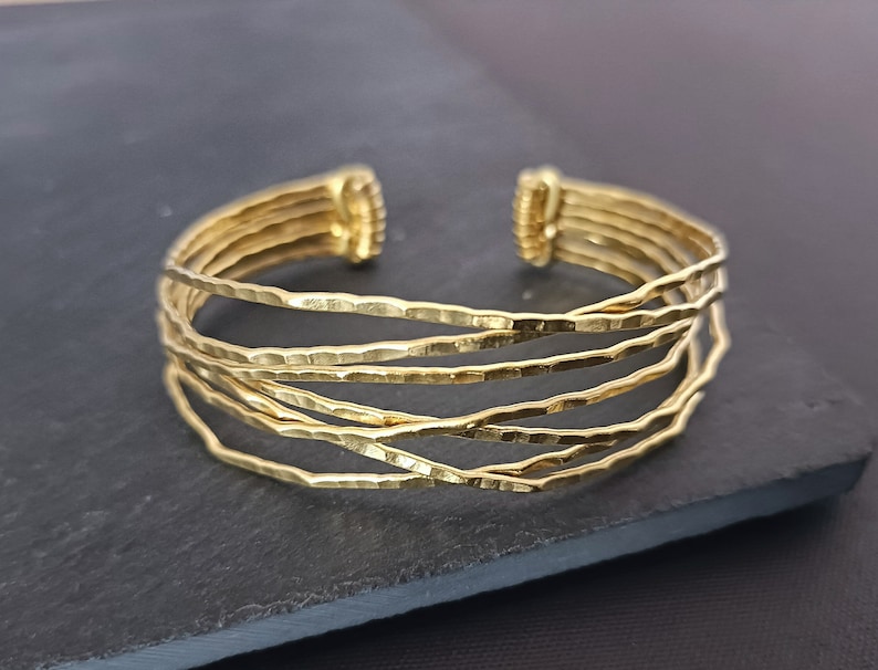May include: A gold-toned multi-strand bangle bracelet with a hammered finish. The bracelet is made of five thin bands of metal that are woven together.