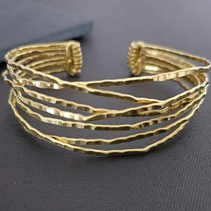 May include: A gold-toned multi-strand cuff bracelet with a hammered texture. The bracelet is made of five thin bands of metal that are woven together.