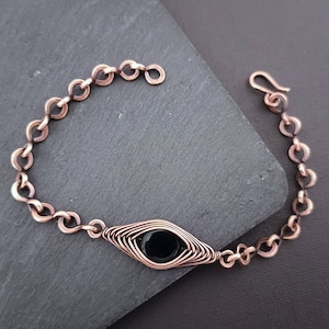 Peut inclure: Un bracelet en chaîne de cuivre avec une pierre précieuse noire sertie dans un motif de fil de cuivre.
