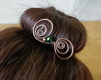 May include: Copper wire hair accessory with a spiral design and a dark green bead. The hair pin is handcrafted and adds a unique touch to any hairstyle. The accessory is shown in a bun.
