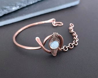 May include: A copper bracelet with a delicate chain and a white opal stone set in a wire-wrapped design.