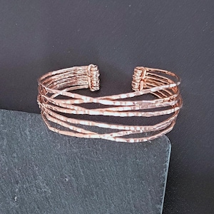 Peut inclure: Un bracelet manchette de couleur cuivr&eacute;e avec un design textur&eacute; et martel&eacute;. Le bracelet pr&eacute;sente plusieurs bandes parall&egrave;les qui se croisent. La conception ouverte du bracelet permet de le porter facilement. Ce bijou convient au quotidien.