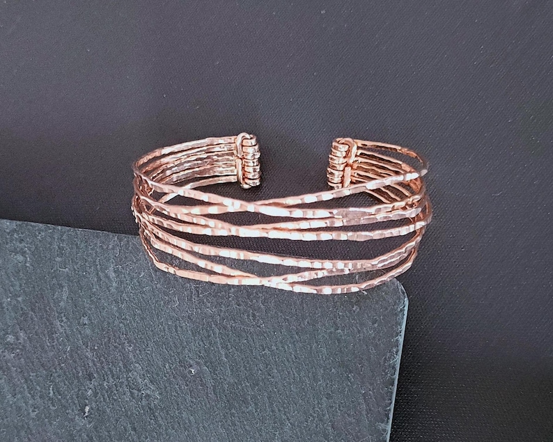 Peut inclure: Un bracelet manchette de couleur cuivr&eacute;e avec un design textur&eacute; et martel&eacute;. Le bracelet pr&eacute;sente plusieurs bandes parall&egrave;les qui se croisent. La conception ouverte du bracelet permet de le porter facilement. Ce bijou convient au quotidien.