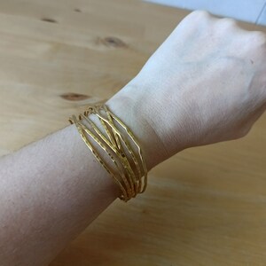 May include: A set of gold-toned bangles stacked on a wrist. The bangles are hammered and have a textured surface.