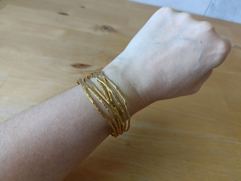 May include: A set of gold-toned bangles stacked on a wrist. The bangles are hammered and have a textured surface.