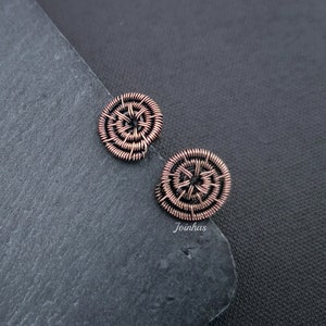 May include: A pair of copper wire earrings with a circular design. The earrings are made of multiple layers of wire that are woven together to create a spiral pattern.
