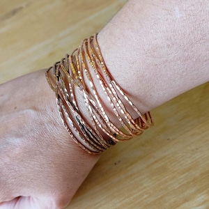 Peut inclure: Plusieurs bracelets fins en cuivre martel&eacute; sur un poignet. Les bracelets ont une surface textur&eacute;e et une couleur brun-rouge&acirc;tre chaude. Les bracelets sont empil&eacute;s, cr&eacute;ant un effet de superposition. Les bracelets sont en cuivre.