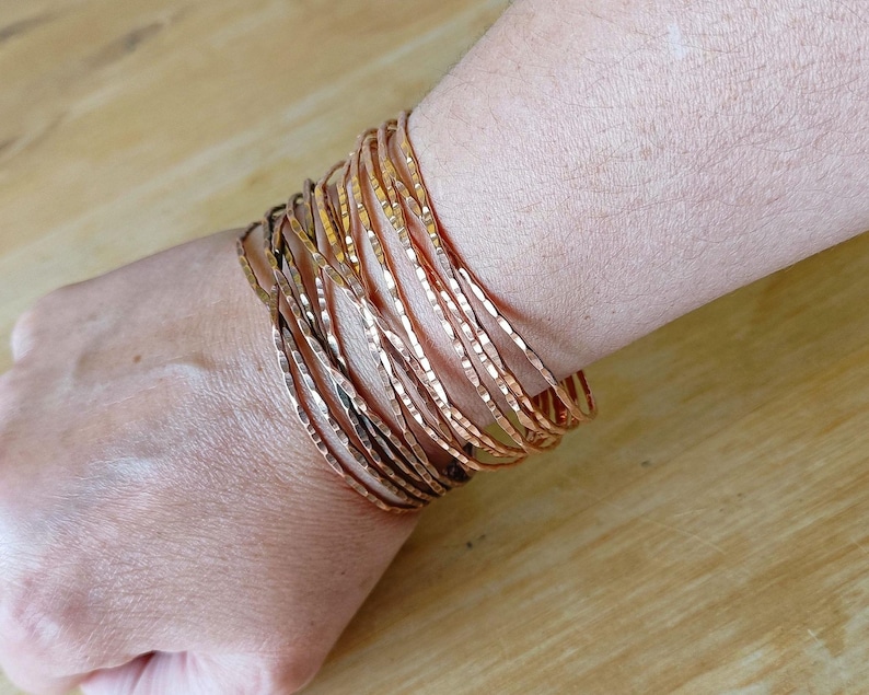 Peut inclure: Plusieurs bracelets fins en cuivre martel&eacute; sur un poignet. Les bracelets ont une surface textur&eacute;e et une couleur brun-rouge&acirc;tre chaude. Les bracelets sont empil&eacute;s, cr&eacute;ant un effet de superposition. Les bracelets sont en cuivre.