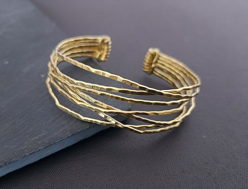 May include: A gold-toned bangle bracelet made of multiple thin, hammered metal bands. The bracelet is open and adjustable.