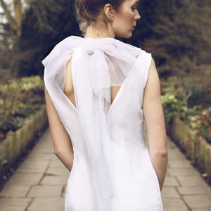May include: A white sleeveless dress with a large white bow at the back of the neck. The dress is fitted and has a simple design.