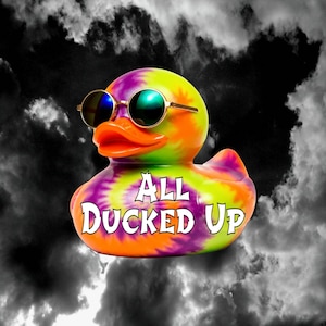 May include: A rubber duck featuring a vibrant tie-dye pattern in shades of yellow, orange, and purple. The duck wears round, gold-rimmed sunglasses with dark lenses and has the text "ALL DUCKED UP" printed in white on its chest area.