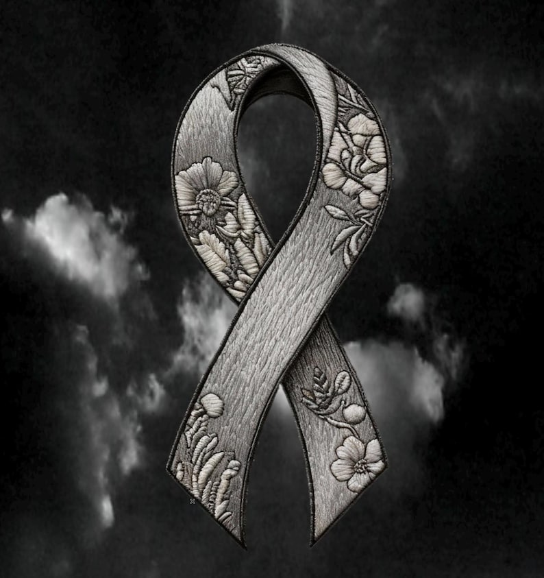 May include: A gray awareness ribbon patch featuring intricate embroidered floral details. The ribbon has a textured surface with stitched flowers and leaves along the edges, finished with a dark border against a dark, cloudy sky background.