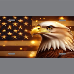 May include: A rectangular license plate featuring a detailed illustration of a bald eagle with a bright yellow beak and white head feathers. The background displays a stylized American flag with golden stars and stripes, accented by soft glowing bokeh lights.