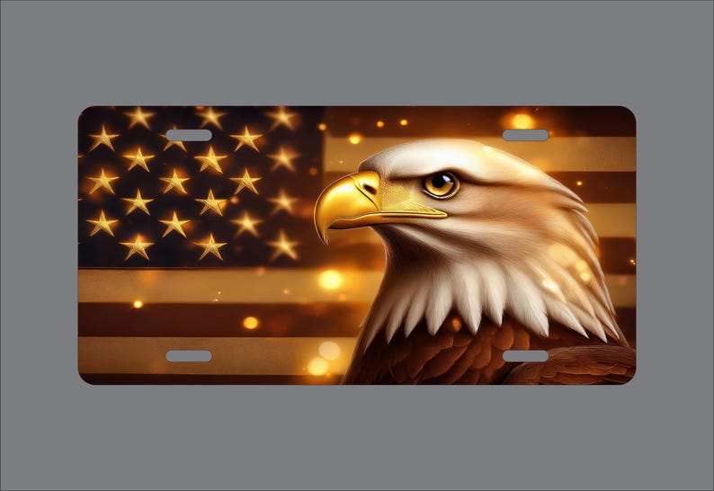 May include: A rectangular license plate featuring a detailed illustration of a bald eagle with a bright yellow beak and white head feathers. The background displays a stylized American flag with golden stars and stripes, accented by soft glowing bokeh lights.