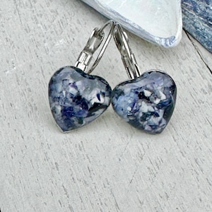May include: A pair of heart-shaped earrings with a marbled blue and white design. The earrings have silver-colored lever-back closures. The earrings are displayed on a light-colored wooden surface.