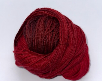 May include: A ball of red yarn, tightly wound, with a gradient of darker red hues in the center. The yarn appears soft and suitable for knitting or crocheting projects. The background is plain white.