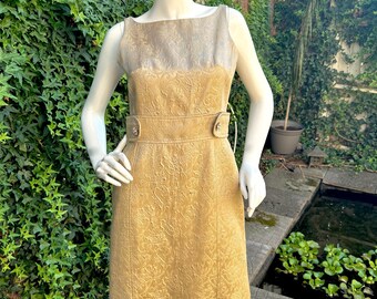 May include: A sleeveless, knee-length dress in a gold brocade fabric. The dress features a square neckline and a fitted waist with a matching belt. The bodice is a lighter gold color than the skirt.
