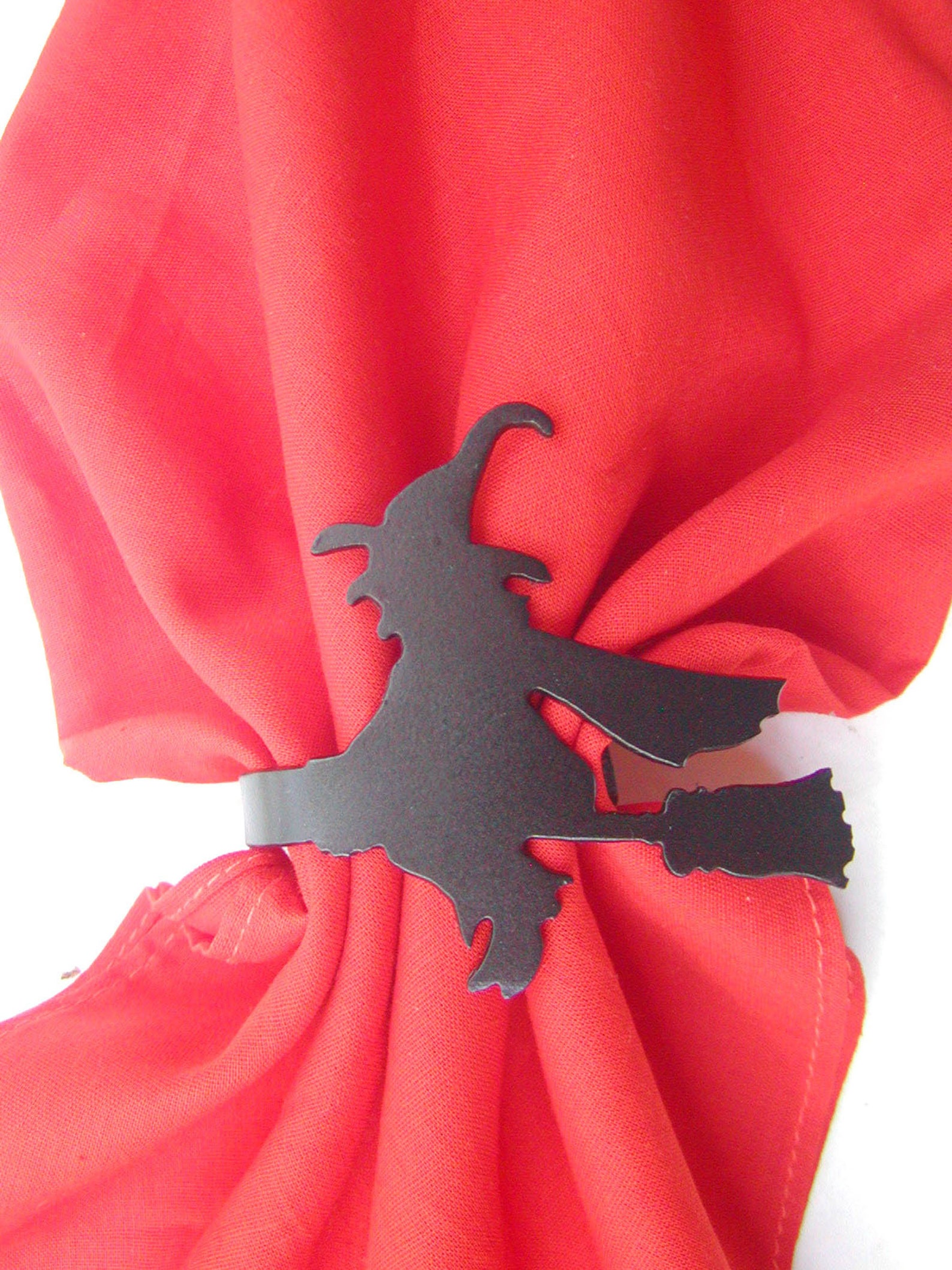 A Dark Witch Silhouette Against Red Cloth Red cloth napkin gathered through a black witch-on-a-broom ring.
