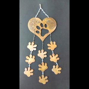 May include: A rustic metal wall hanging featuring a heart shape with a paw print cutout. Below the heart, several paw print cutouts dangle from chains. The metal has a weathered, bronze-like finish, creating a charming, pet-themed decoration.