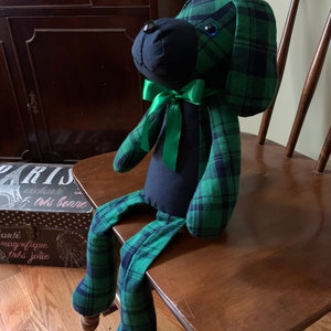 Puede incluir: Un perro de peluche con cuerpo negro y tela de cuadros verde y negro. El perro tiene un lazo verde y ojos azules.