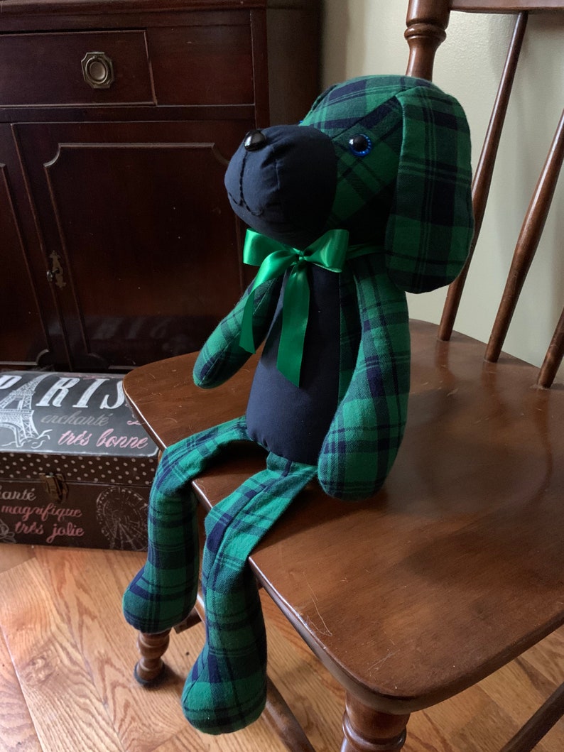 Puede incluir: Un perro de peluche con cuerpo negro y tela de cuadros verde y negro. El perro tiene un lazo verde y ojos azules.
