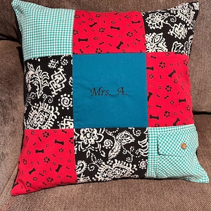 May include: A square patchwork pillow featuring nine distinct fabric panels. The design includes red fabric with black bone and paw prints, black fabric with white floral patterns, teal fabric with the embroidered text Mrs. A., and teal gingham.