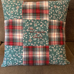 May include: A square throw pillow featuring a patchwork design of teal fabric with a small floral pattern and red, white, and black plaid fabric. The center teal panel is embroidered with the red text "Love, Grandma & Grandpa".