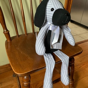 Puede incluir: Un perro de peluche rayado gris y blanco con orejas negras y una cara negra. El perro est&aacute; sentado en una silla de madera con una cinta blanca alrededor del cuello.