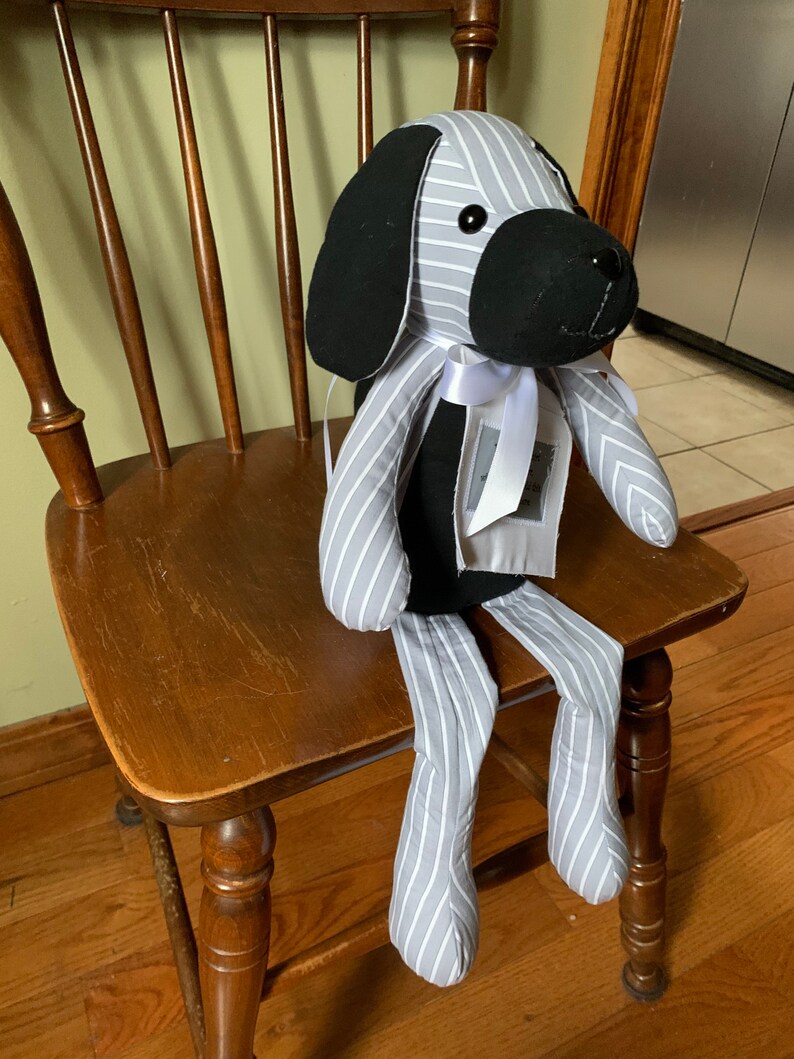 Puede incluir: Un perro de peluche rayado gris y blanco con orejas negras y una cara negra. El perro est&aacute; sentado en una silla de madera con una cinta blanca alrededor del cuello.