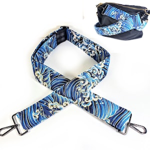 Peut inclure: Sangle de bandoulière réglable à motif de vagues bleues et dorées avec des ferrures argentées. La sangle est en tissu et présente un motif tissé.