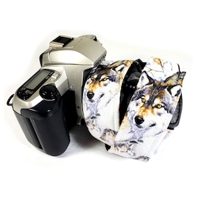 May include: A silver camera with a wolf-themed camera strap. The strap is white with brown and gray wolf images.