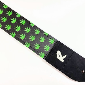 Op de afbeelding: Zwarte gitaarband met een groen marihuanabladpatroon en een wit "R"-logo.