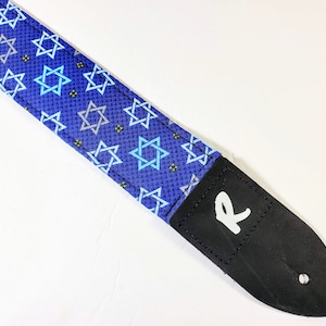 May include: Blue guitar strap with a pattern of white and blue Stars of David. The strap has a black leather end with a white "R" logo.