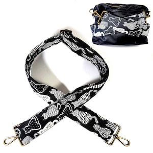 May include: Black and white patterned adjustable shoulder strap with gold metal hardware. The strap features a repeating pattern of stylized cats.