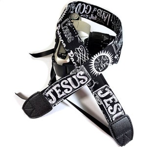 May include: Black and white camera strap with the words "JESUS", "LAMB of GOD", "BREAD of LIFE" and other religious text printed on it.